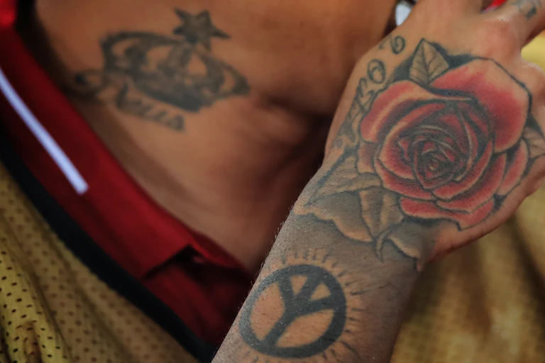 A man wtih tattoo of a red rose on his hand and a tattoo of a crown on his neck.