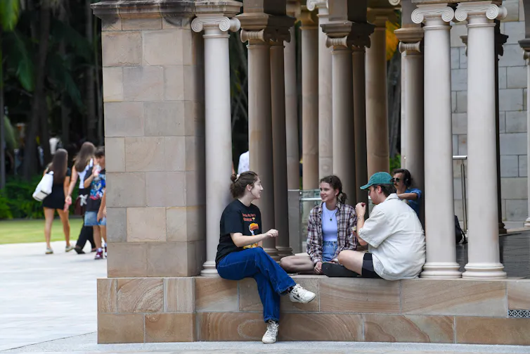 Three casually dressed university students sitting cross legged surrounded by concrete blocks.
