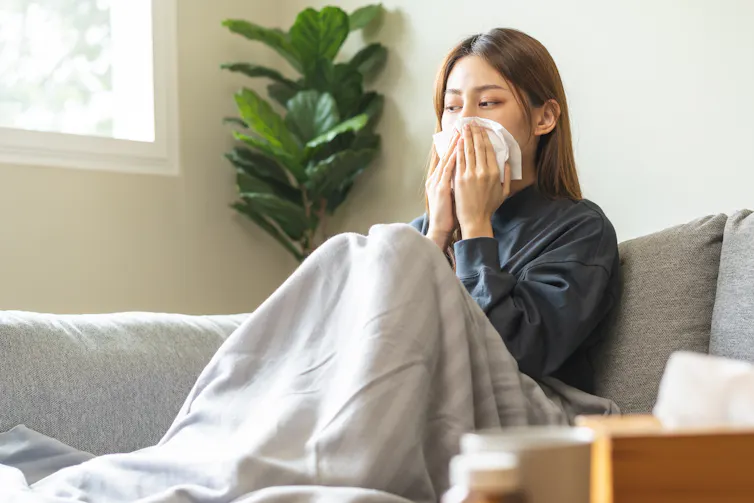 A woman sitting on a couch blowing her nose.