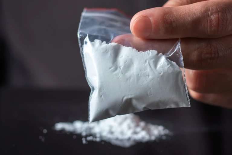 Hand holding plastic baggie of white powder, with powder on black surface