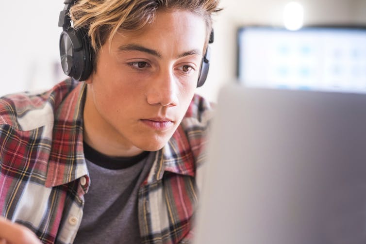 A teenage boy wearing headphones, looking at a screen.