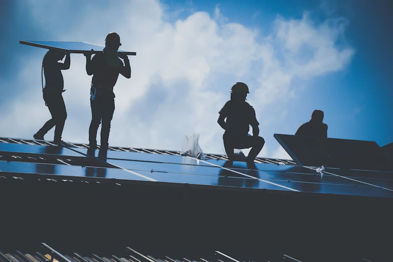 Four figures in the shade installing solar panels on a roof.