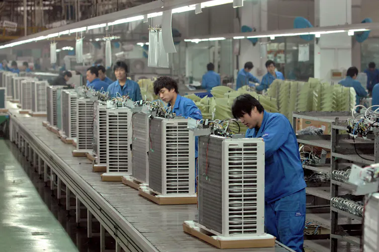 Workers in blue overalls attend erect plastic rectangles.