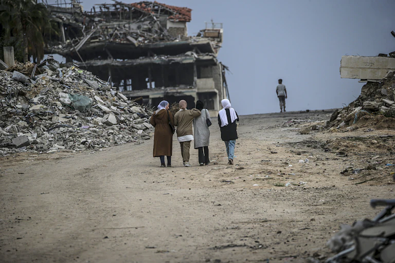 A group of internally displaced Palestinian women walk along a war-damaged street in Gaza City.
