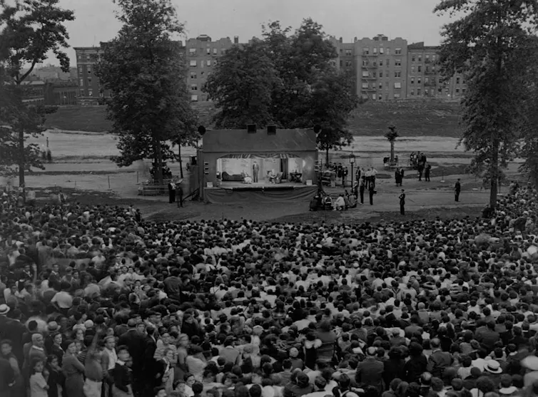 Black-and-white photograph of large crowd gathered in a public park to watch a play.