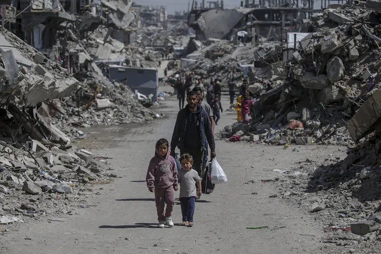 Palestinians walk past the rubble of destroyed buildings.