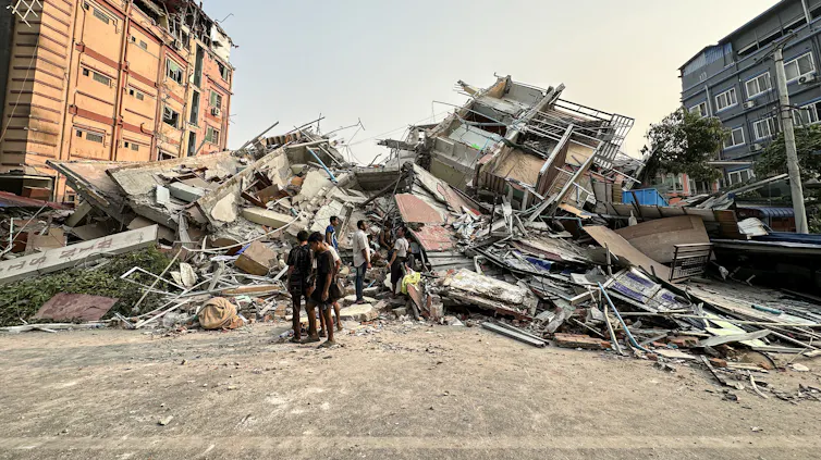 People stand in front of the rubble of a building.