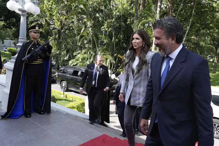 A woman wearing a blazer walks up steps, next to a man in a black suit.