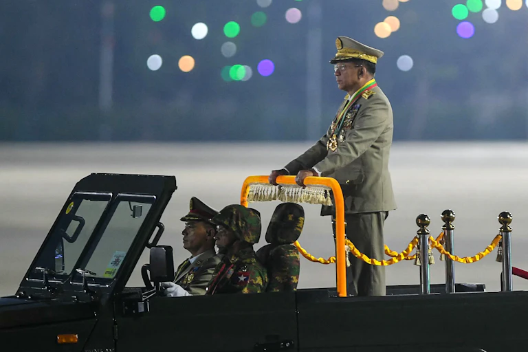 A man in military garb stands on a military vehicle.