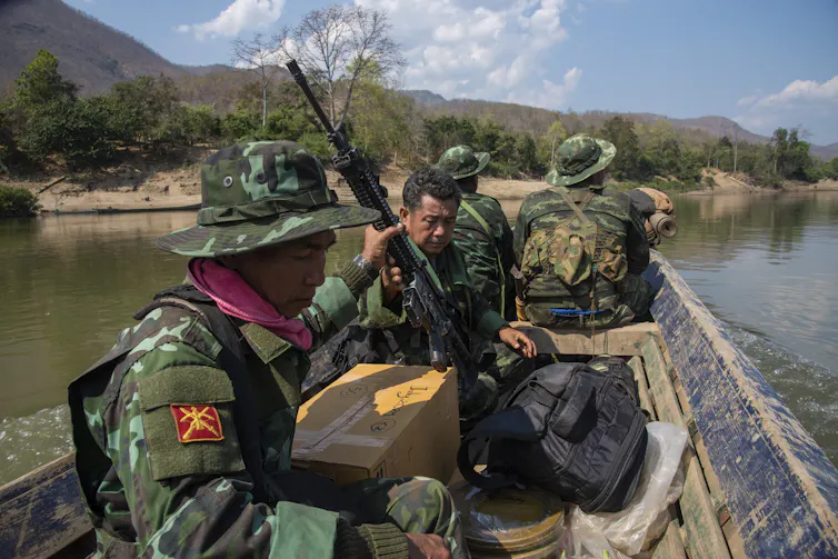 Men in army fatigues sit on a boat in a river.