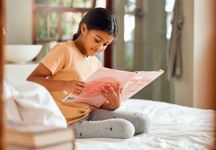 Girl reads a picture book on her bed.