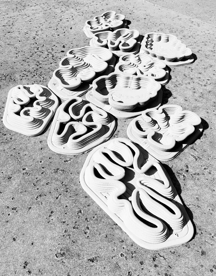 Ten grey swirling organically shaped objects laid together on ground