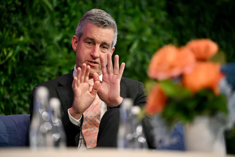Photo of a man in a suit holding his hands up in front of him.