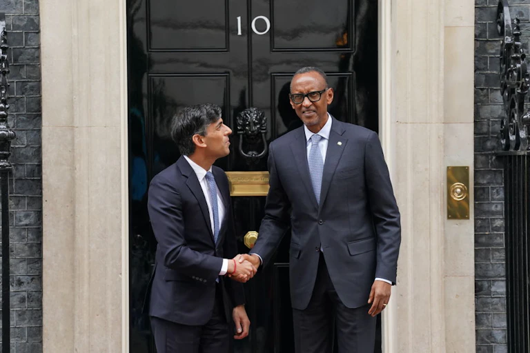 Two men shake hands in front of a door with the number 10 on it