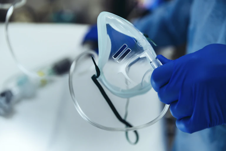 Hand in a blue glove holding a plastic tube which appears to be a medical drip