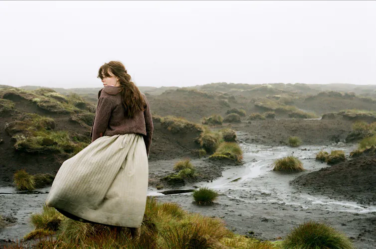 A woman in 18th century clothing stood by a brook.