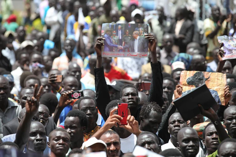 A crowd of people cheering with their hands held up, with some holding up photographs and others phones