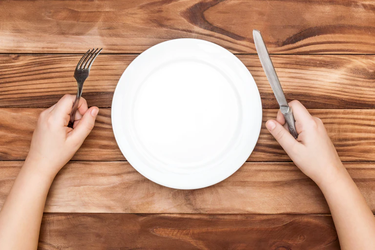 An empty plate. A person holds a fork and knife on either side of it.