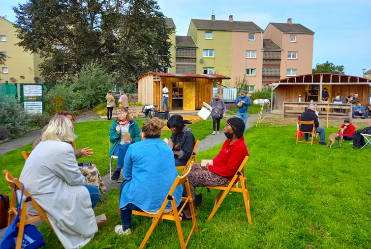 people sat on chairs in community garden eating lunch, housing buildings in background
