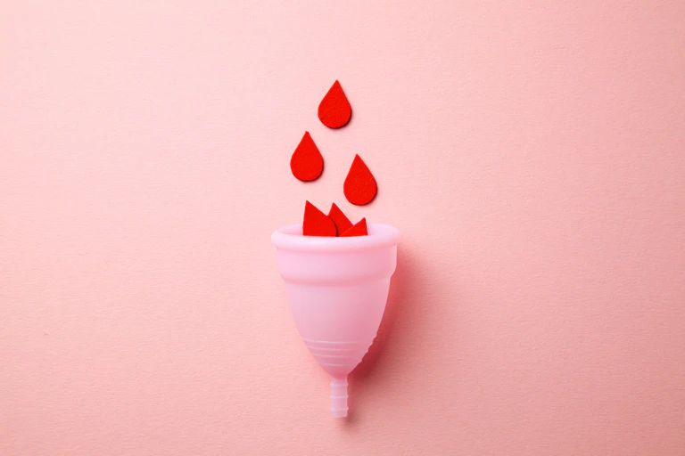 A pick menstrual cup with paper cut-outs of red blood flowing into it.