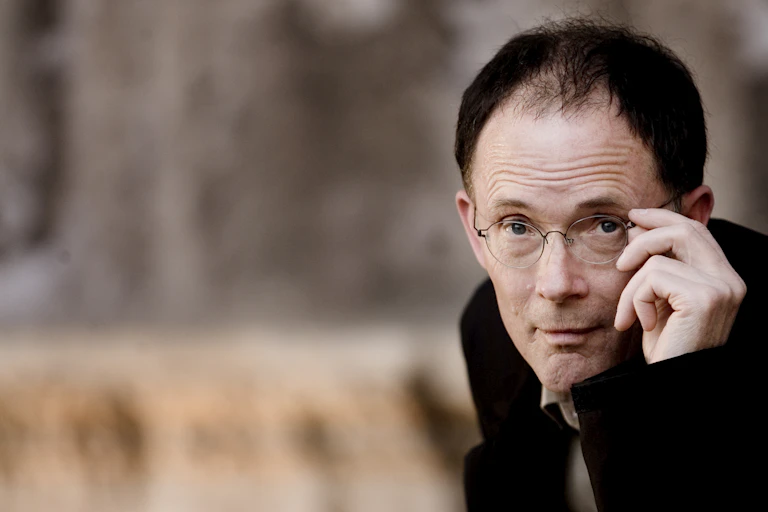 Balding man poses while adjusting his glasses.