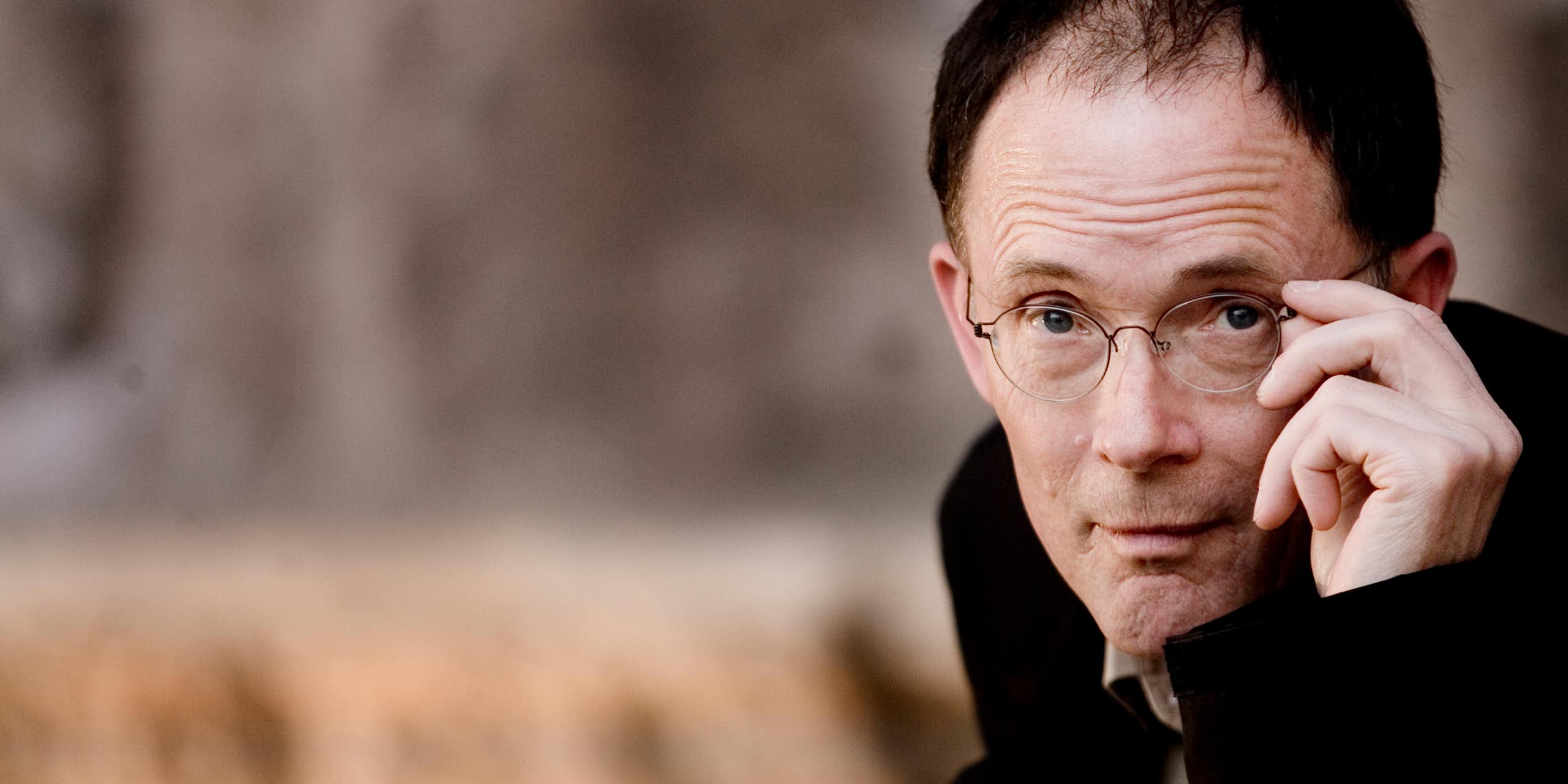 Balding man poses while adjusting his glasses.