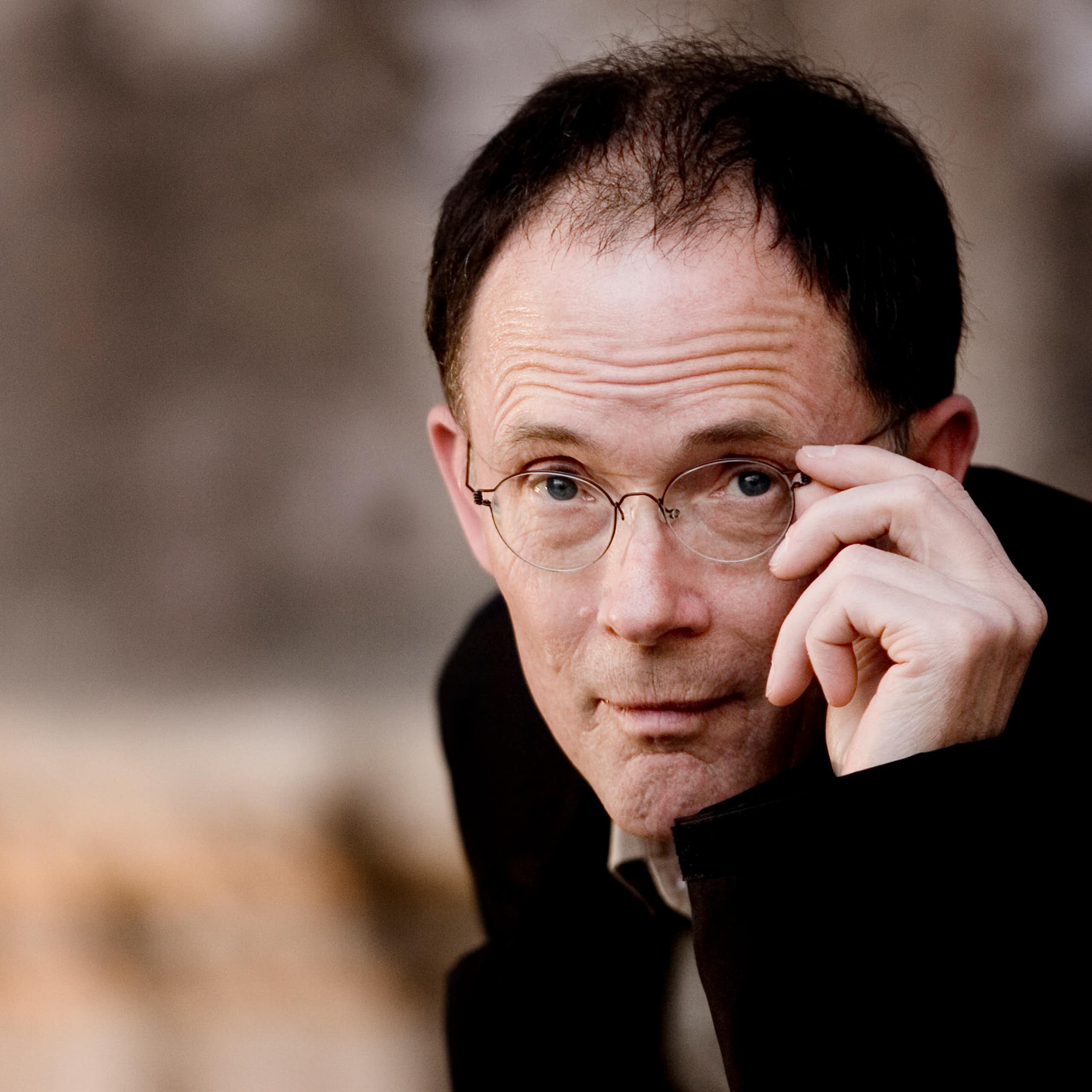 Balding man poses while adjusting his glasses.