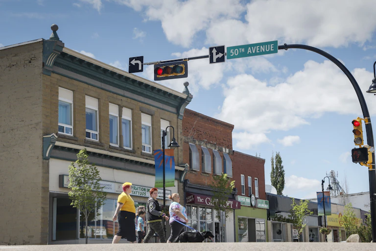 People cross the street in a rural community under sunny skies.