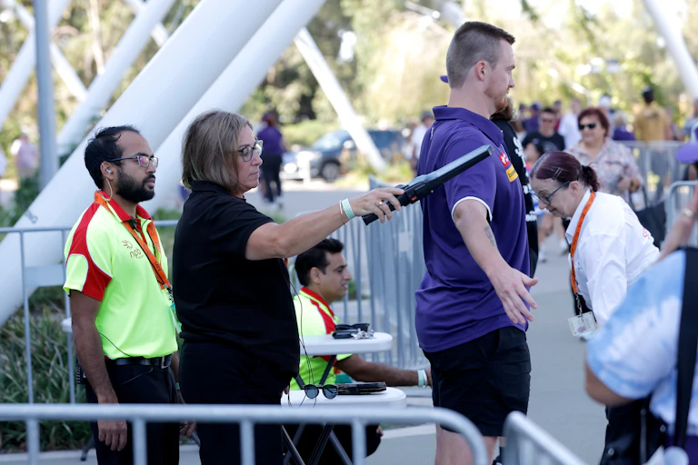 A security guard uses a security scanner on a patron ahead of an AFL game