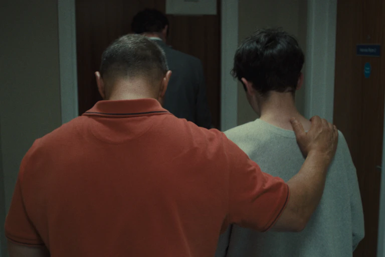 A man in orange T shirt and a boy in white T shirt seen from behind.