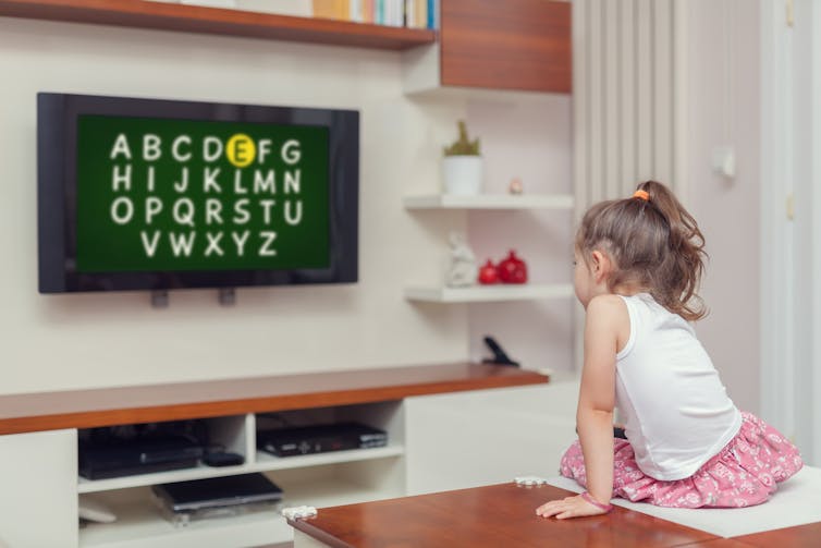 A young girl watches a program on the TV featuring the alphabet.