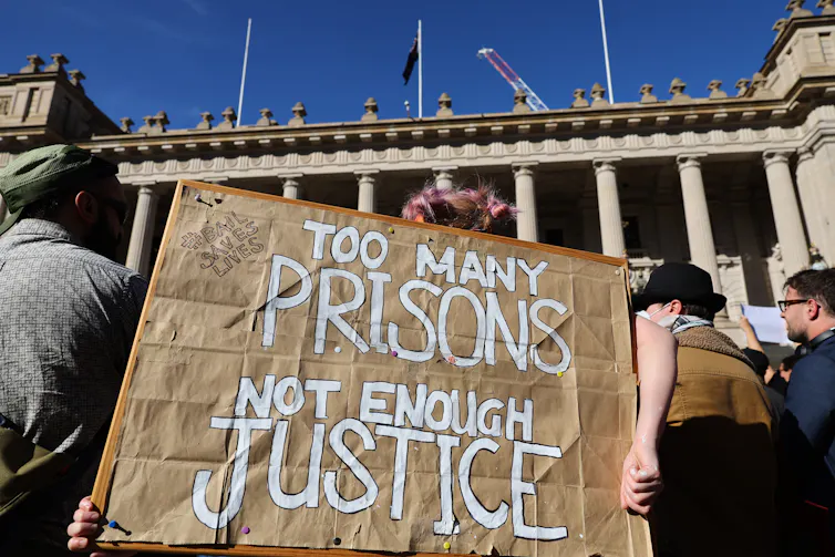 A cardboard sign that says too many prisons not enough justice.