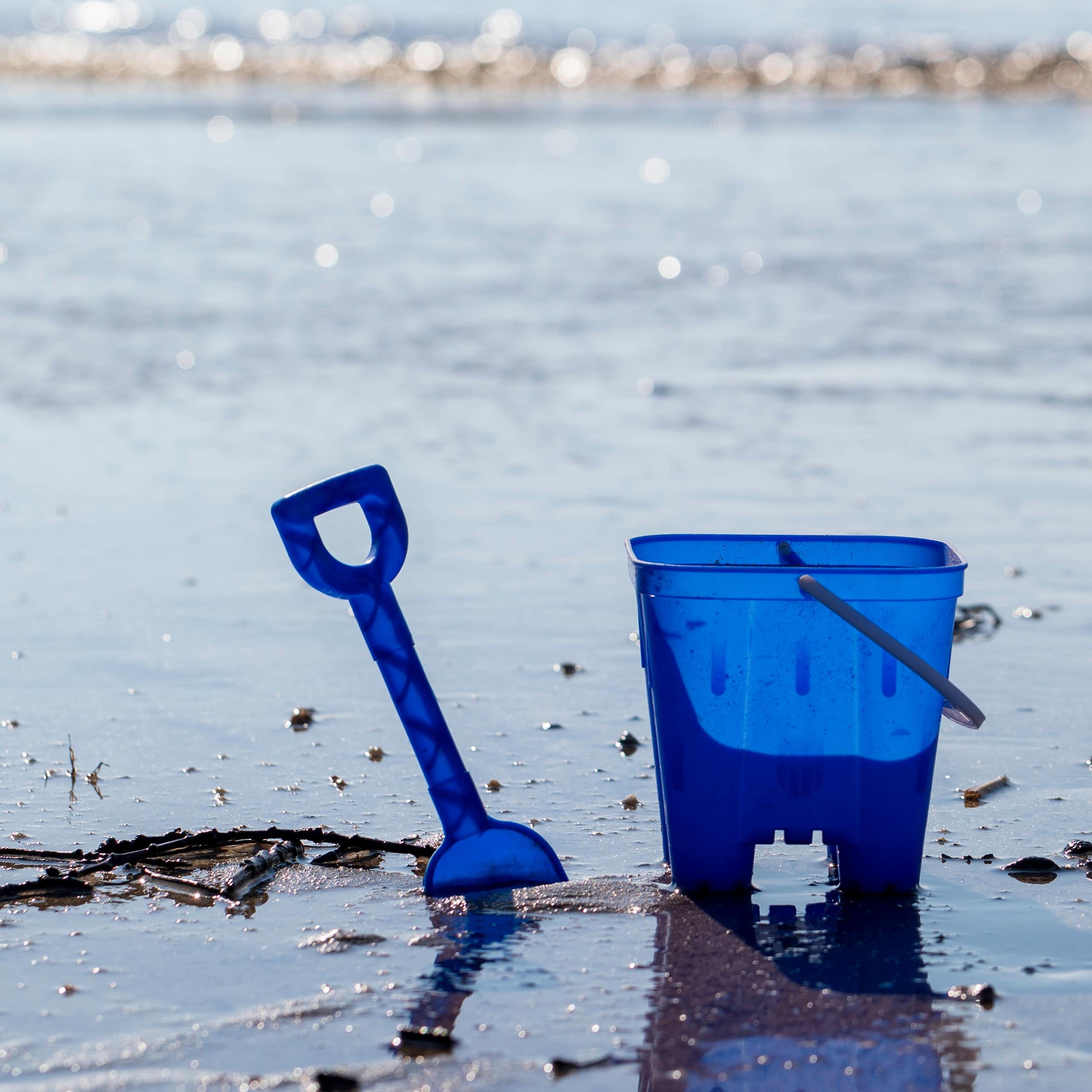 A blue bucket and spade on a beach.