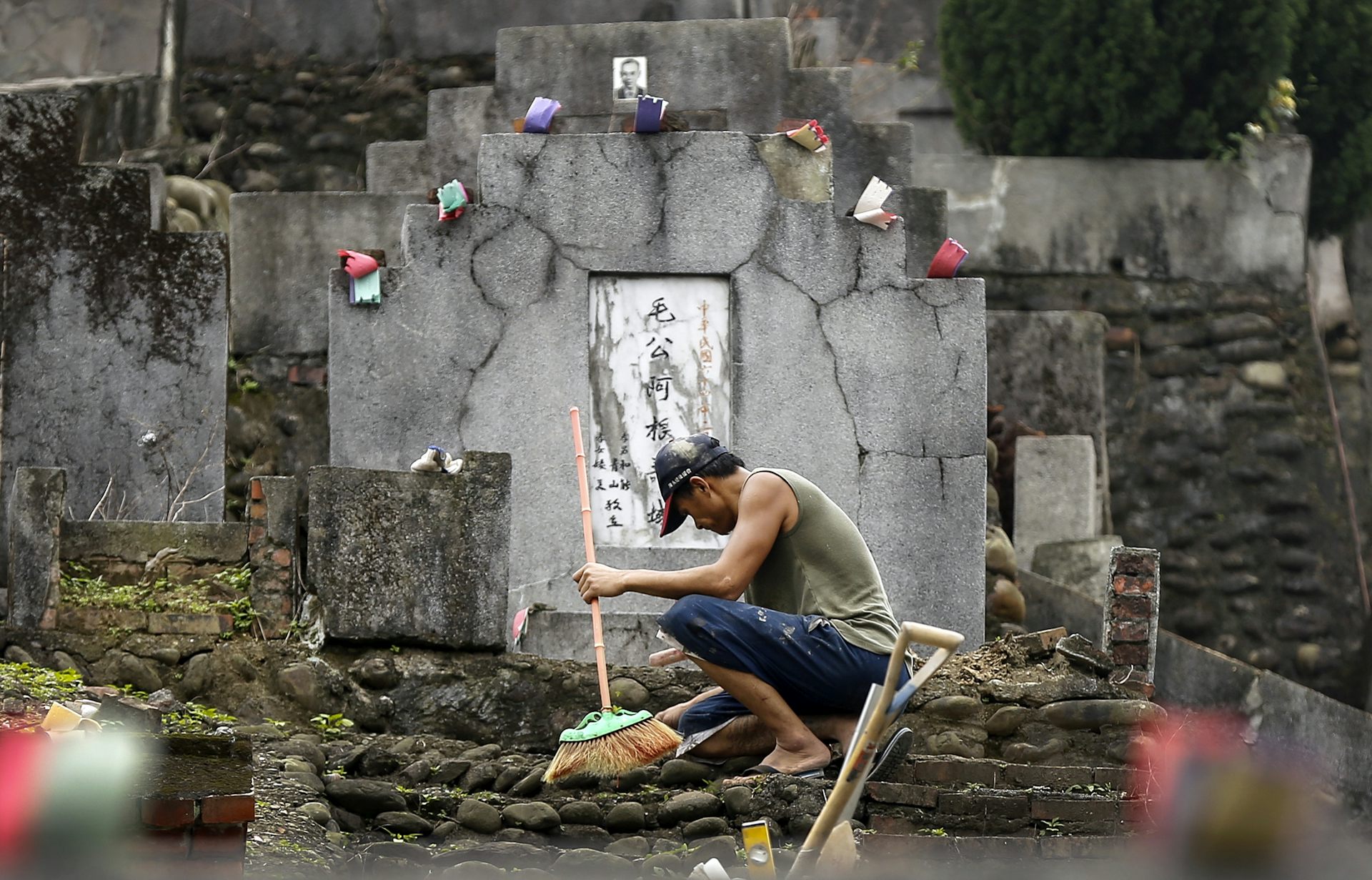 Man crouching by a grave holding a broom