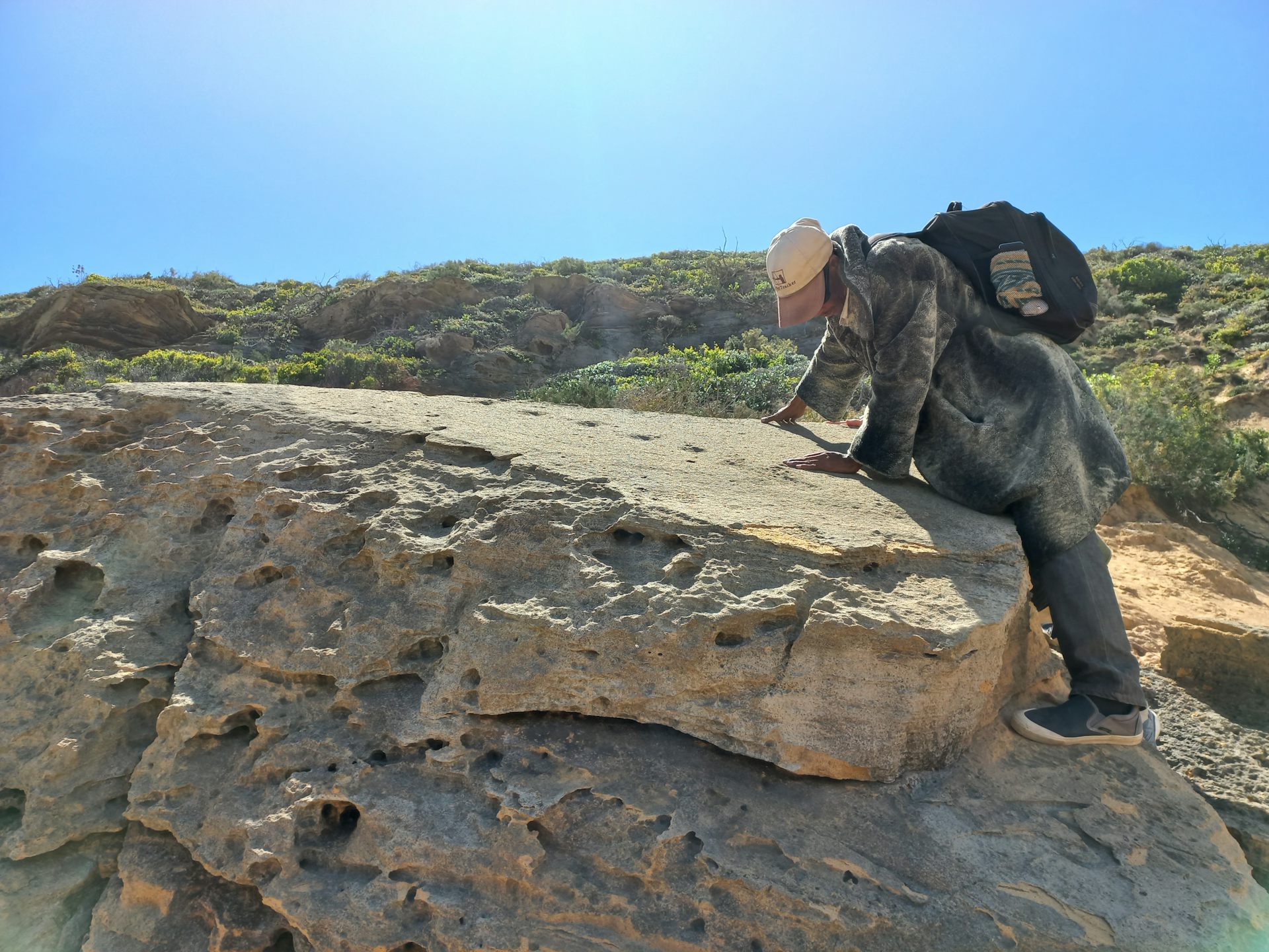 A man stands on a rocky slab, looking at marks on the top surface