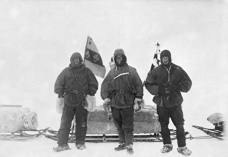 Three men in the snow with sledges behind them