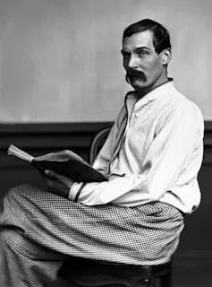 A man with a strong moustache reading a book