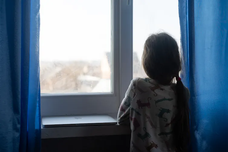 View from behind of a young girl staring out a window