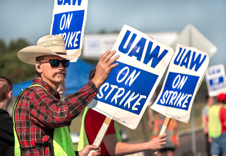 Man in a cowboy hat holding a sign saying 'UAW on strike'.