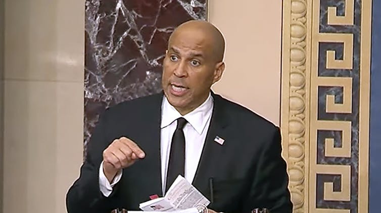 Trump, interrumpido: discurso de 25 horas del Cory Booker de 25 horas para la acción colectiva 1 El hombre se encuentra en el podio e indica el documento