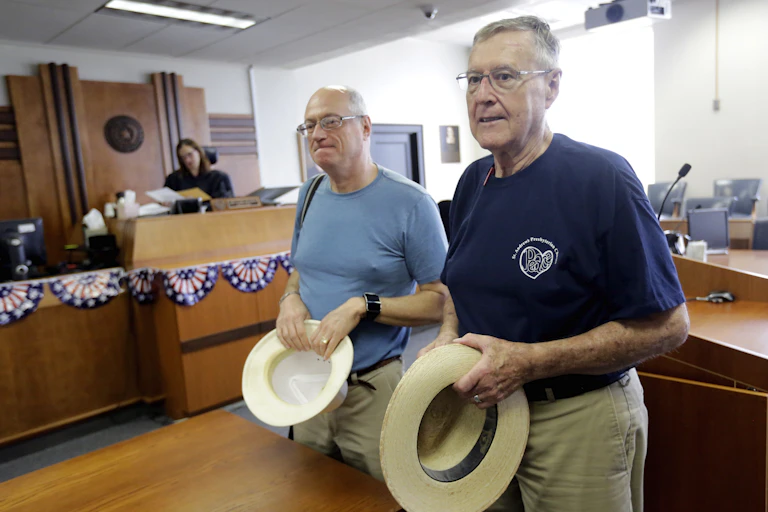 Two men in an office, holding hats.