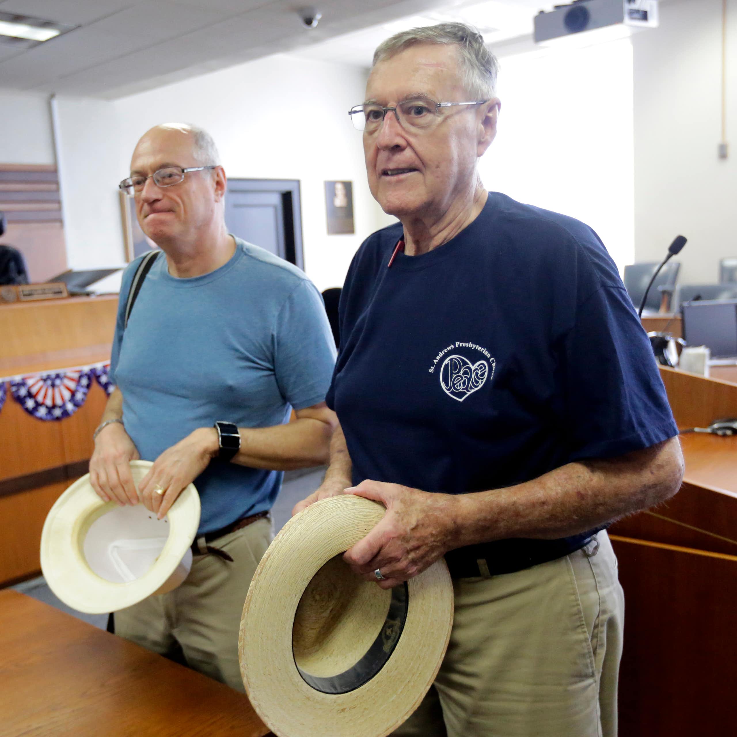 Two men in an office, holding hats.