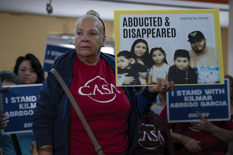 A woman dressed in a red tshirt hold a sign protesting the deportation of a U.S. immigrant.
