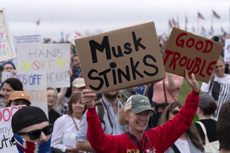 Uma mulher segura um cartaz onde se lê Musk Stinks.