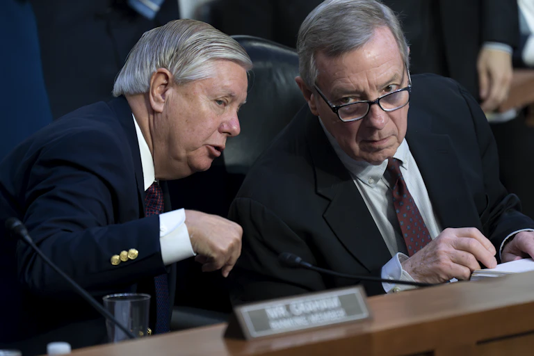 Two older men in business suits lean toward each other.