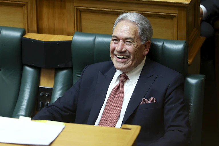Winston Peters sitting in parliament, smiling.
