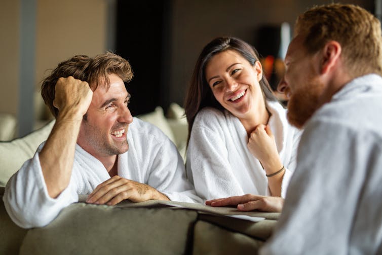 Two men and a woman, all dressed in dressing gowns, chat happily.