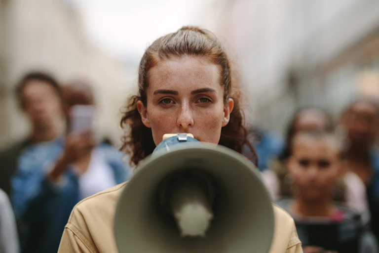 Ativista feminina protestando com um megafone durante uma greve, com um grupo de manifestantes ao fundo.
