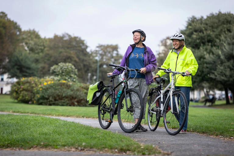 Two older people walk their bikes
