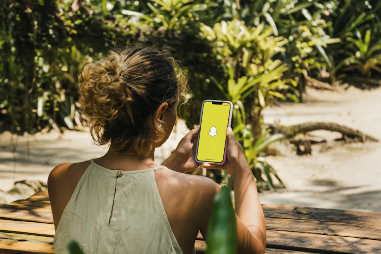 Girl in a park holding a smartphone with Snapchat app on the screen.